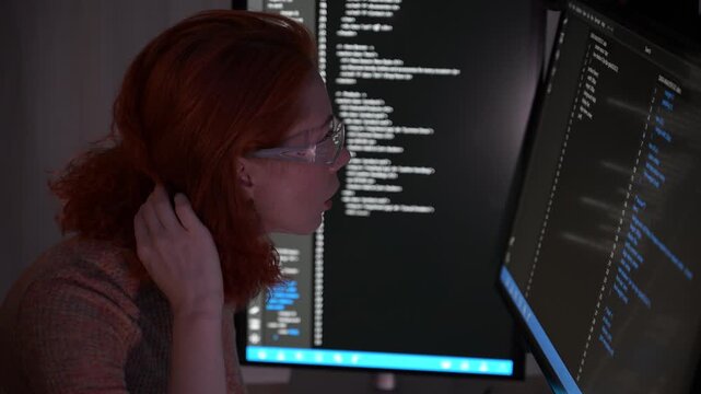 Focused female software developer coding at night in a modern workspace, wearing glasses and analyzing code on computer screen. Concept of programming, technology, cybersecurity, and digital innovatio