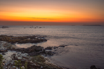Vibrant sunset over the Atlantic Ocean near Guernsey, Channel Islands, with deep orange and red sky reflecting on calm water. © Tadeas