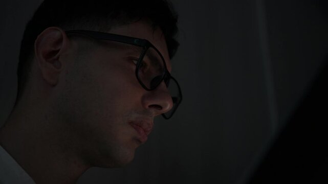 Focused young female software developer programming code on multiple monitors in a dark home office at night. Professional woman engineer working on cyber security and data science tech project.
