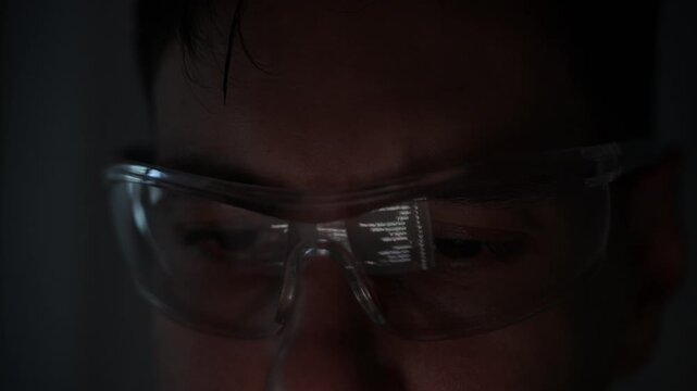 Focused young female software developer programming code on multiple monitors in a dark home office at night. Professional woman engineer working on cyber security and data science tech project.