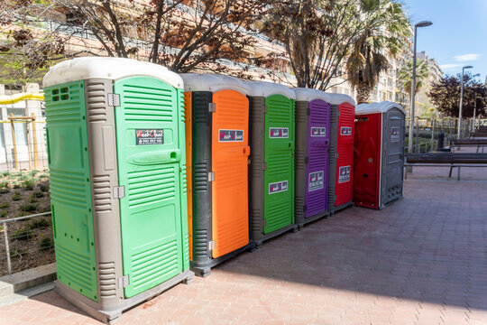 Fila de lavabos port&aacute;tiles de colores instalada en un espacio p&uacute;blico durante un evento al aire libre en Barcelona.