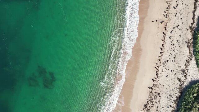 Aerial drone view of ocean waves gently hitting a sandy beach along the Normandy coast in France. Natural coastal landscape with a calm and relaxing atmosphere, ideal for travel, tourism and backgroun