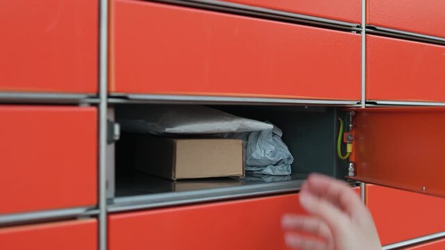 Hand placing a box and envelopes into an orange automated parcel locker for shipment. Close-up of the delivery process and self-service logistics. High quality 4k footage