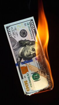 One hundred dollar bill on fire against a black background symbolizing financial loss, inflation and economic crisis