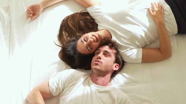 A happy couple enjoys a peaceful morning, lying comfortably in bed and smiling. Their loving relationship is evident in their relaxed expressions.