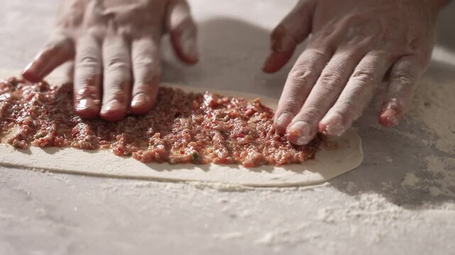 Male hands spreading minced meat on a long flat dough for making a traditional Turkish pide, fa01