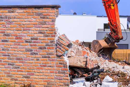 Construction workers demolish a brick wall near a building site in a city on a sunny day