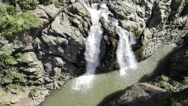 Drone hovers over Lusushwana River as camera pans up over both tiers of Mantenga Waterfall on a sunny day in Ezulwini, Eswatini