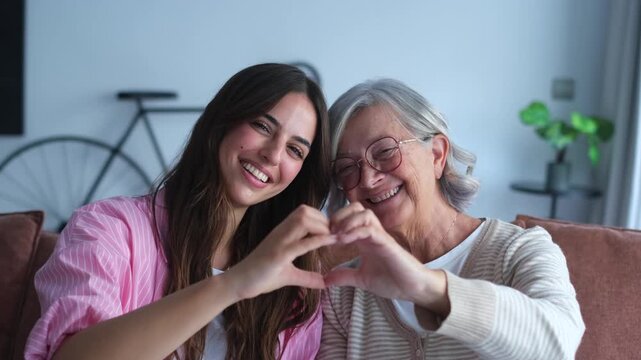 Granddaughter and grandmother share a loving moment, smiling and creating a heart shape with their hands. This heartwarming scene represents family love, happiness, and a strong intergenerational bond