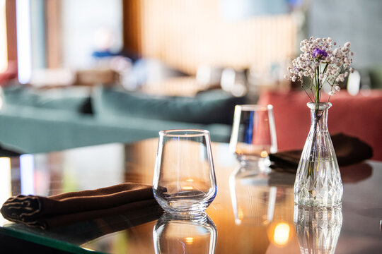 Empty glass on served restaurant table with flower vase. Elegant interior setting for fine dining lunch or romantic dinner.