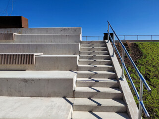 Obraz premium Modern Concrete Outdoor Amphitheater Seating and Staircase with Metal Handrail under Clear Blue Sky, Urban Public Space Architecture and Contemporary Landscape Design