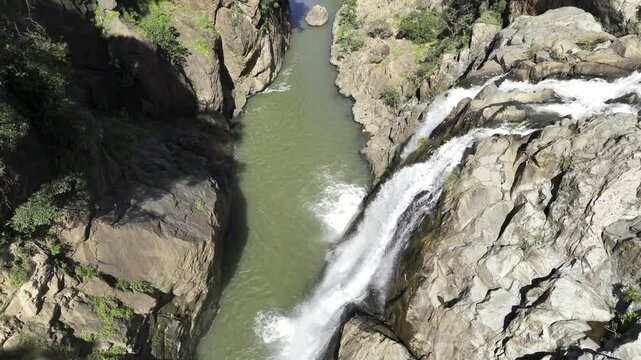 Drone flies along Lusushwana River as camera pans up from Mantenga waterfall to reveal river cutting through forested valley on a sunny day in Ezulwini, Eswatini