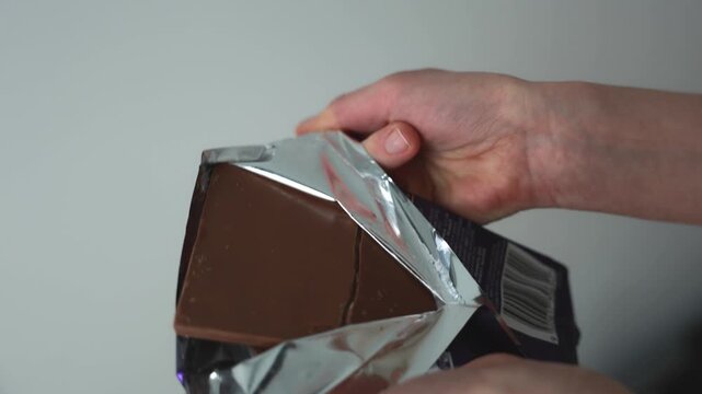 Hands unwrapping chocolate bar, opening packaging and preparing to eat