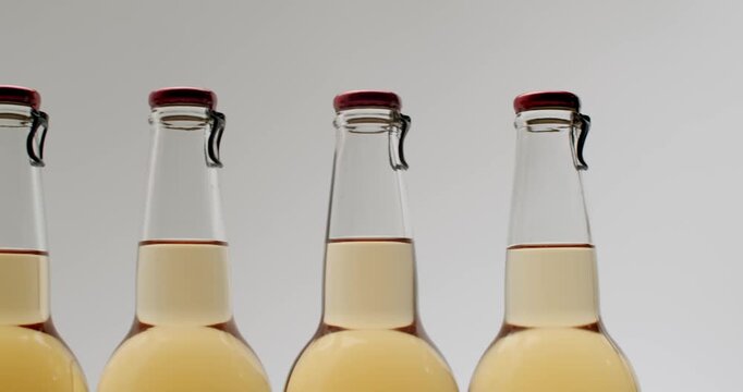 Several swing-top bottles filled with golden craft beer rotating on a surface with wheat ears and barley grains. Light reflects off the clear glass showing the different colors of the beverage