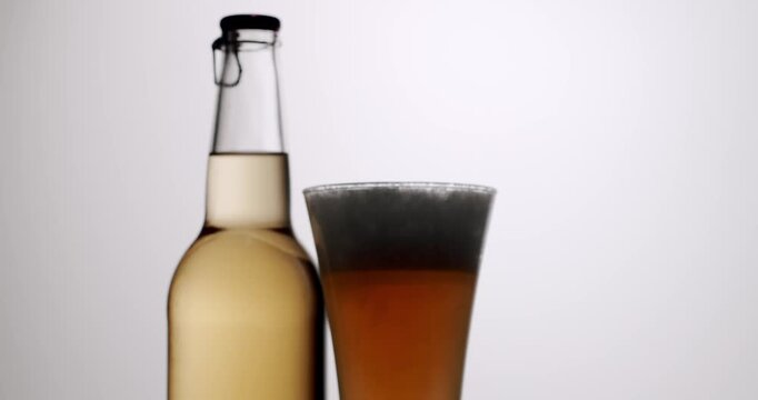Fresh glass of dark beer with a thick head of foam standing next to a bottle on a white background. Slow-motion footage showing the amber-colored ale in a clean, minimalist studio setting