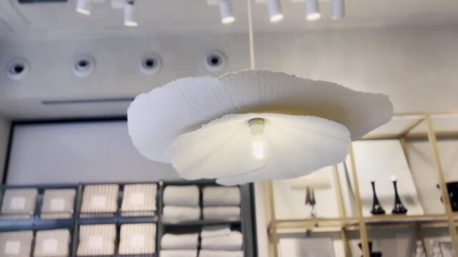 Stylish white paper chandelier with a wavy, floral-like design hanging from the ceiling, illuminating a modern home decor store with shelves of linens and decorative items in the background