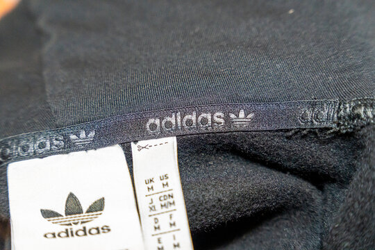 Warsaw, Poland - April 20, 2026: Close-up view of an Adidas clothing label showcasing sizing information and brand logo, presenting a high-quality fabric texture and branding elements.