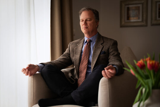 Confident middle-aged man meditating in an armchair at home
