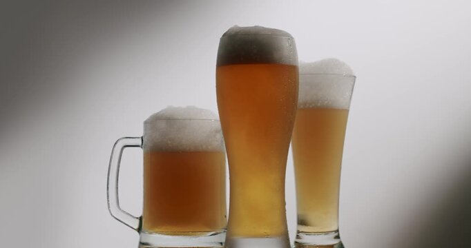 Different types of beer glasses, including a pint, a mug, and a pilsner glass, standing with foamy heads on a white background with a subtle shadow, capturing the essence of refreshment