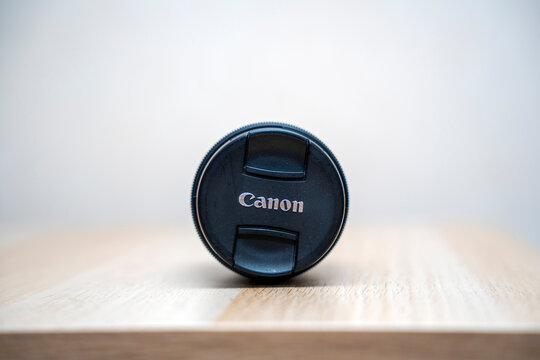 Warsaw, Poland - April 20, 2026: Close-up of a Canon camera lens cap on a wooden surface, representing photography tools and lifestyle. Ideal for marketing and promotional use.