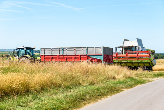 Combine harvester and a trailer pulled by a tractor stationary in a field on a clear summer day