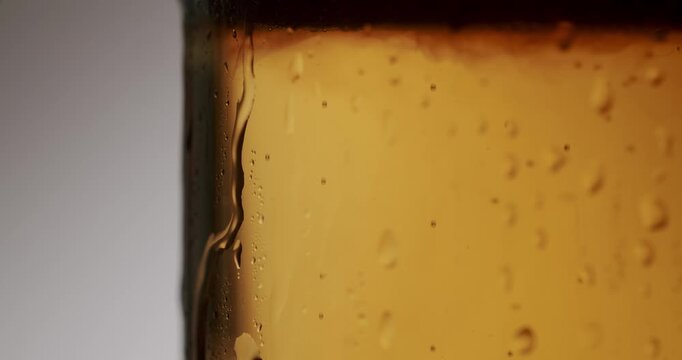 Extreme close-up of a refreshing glass of cold light beer with condensation droplets slowly running down its side, showcasing the beverage's carbonation and crisp, golden color