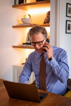 Mid-aged man with laptop and smartphone sitting at desk and working from home