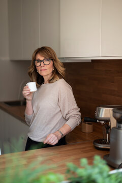 Confident blond haired woman standing in her modern home and drinking a coffee