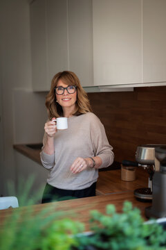 Confident blond haired woman standing in her modern home and drinking a coffee