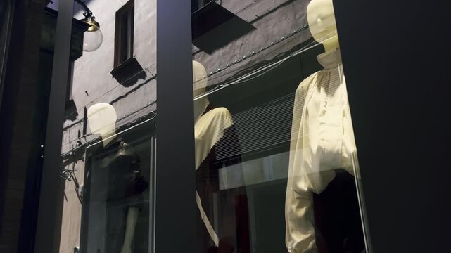 Mannequins showcasing a sophisticated and stylish clothing collection behind a glass storefront, with the reflection of a quiet city street creating an evocative and urban atmosphere