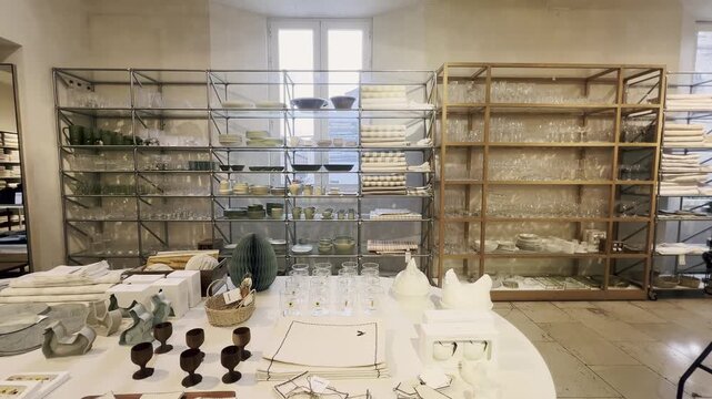 Stylish interior of a retail shop showcasing a wide variety of contemporary kitchenware, including ceramic dishes, glassware, and table linens elegantly arranged on shelves and a central table