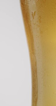Extreme close-up of a cold, crisp beer in a glass covered with condensation, with a single water droplet trickling down the side in refreshing slow motion against a clean white background. Vertical