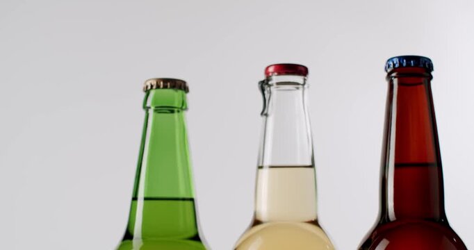 Three different colored glass bottles of craft beer and cider rotating in slow motion, showing an assortment of refreshing alcoholic beverages isolated on a clean white background