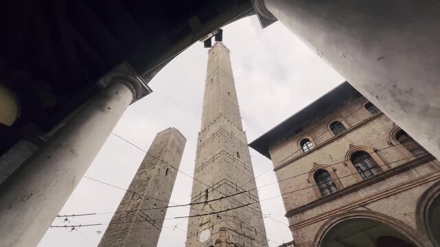 Low-angle view of the medieval Two Towers, Asinelli and Garisenda, symbols of Bologna, Italy, with ancient architecture and arcades against a cloudy sky on an overcast day