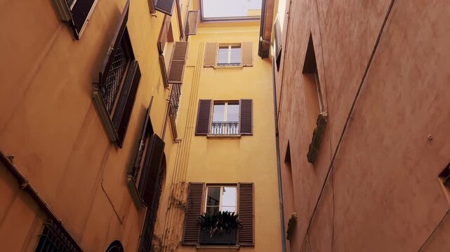 Low-angle tilting shot revealing a charming narrow alley with traditional ocher-colored buildings, wooden shutters, and an old arched doorway, capturing the essence of historic european urban life
