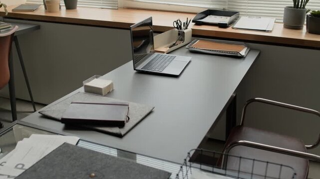High angle no people tilt down shot of office desk with a laptop, a notebook, a desk organizer, and plants on the windowsill