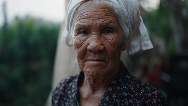 Weathered elderly asian woman wearing traditional headscarf, expressing quiet dignity with soft facial lines revealing deep personal history and cultural heritage