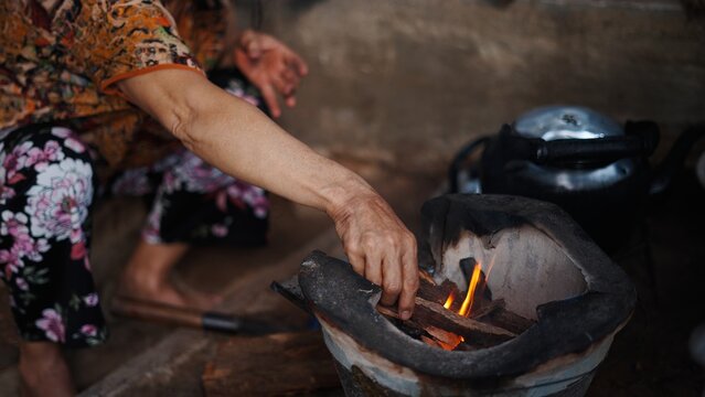 Elderly woman stoking wood burning stove, preparing traditional meal in rural kitchen setting