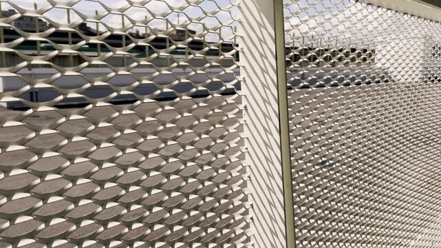 Modern building facade detail featuring a perforated metal sheet panel with a diamond pattern, creating an abstract architectural background with moving light and shadow