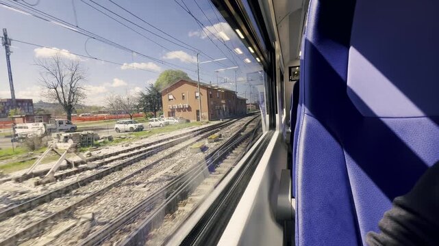 Passenger view from a high-speed train window leaving the Bologna Centrale railway station in Italy, with the industrial landscape and railroad tracks moving past on a sunny day