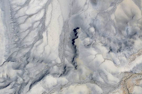 Aerial view of the intricate textures and eroded grey badlands with deep shadows and dry riverbeds in Caineville, Utah, United States.