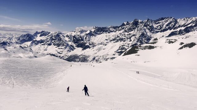 Majestic alpine scenery with skiers gracefully gliding down a vast, sun-drenched slope in the Italian Alps, surrounded by towering snow-capped peaks under a clear blue winter sky