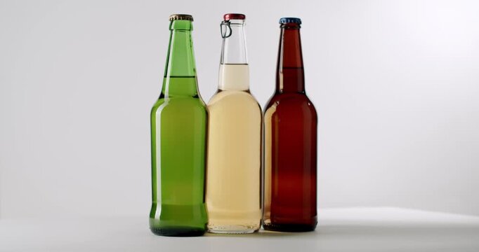 Three different colored glass bottles of fresh craft beer with light and dark lager rotating on a turntable isolated on a white background, perfect for showcasing a brewery's product range