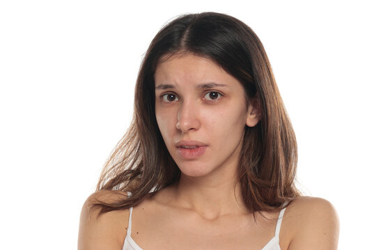 Studio shot of a young brunette woman in white top looking scared and frightened, no makeup portrait on white background