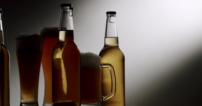 Various types of craft beer in bottles, glasses, and mugs arranged together in a backlit setting with dramatic lighting, creating elegant silhouettes as the camera slowly pans across