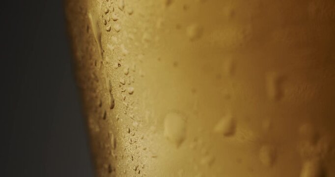 Close-up of a refreshing cold light beer pouring into a sweating glass, creating a frothy head of foam and causing condensation droplets to trickle down the side in slow motion