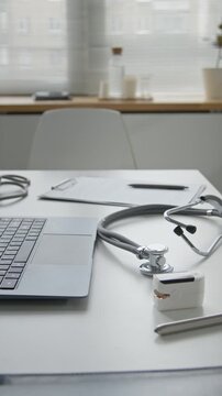 Vertical panning shot of medical diagnostic equipment resting on doctors desk with open laptop at modern clinic