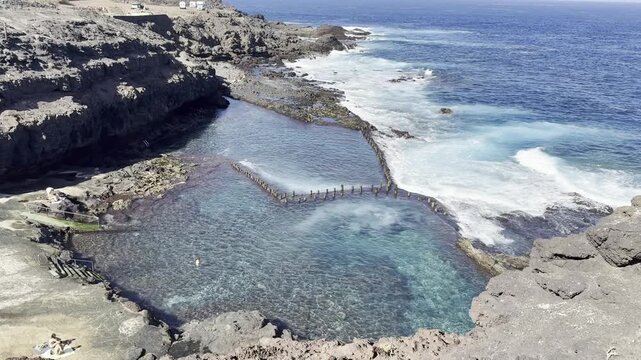 Natural volcanic rock pool Roque Prieto on the Atlantic Ocean coast in Gran Canaria, Canary Islands, Spain. Dramatic lava formations, crystal clear water and rugged coastline - stunning seascape.