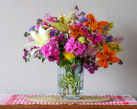 Colorful summer bouquet with lilies and garden flowers in glass vase on table, bright floral arrangement, home decor still life