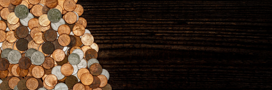 Coins are arranged in a pile on a dark wooden surface showing different denominations and sizes of currency